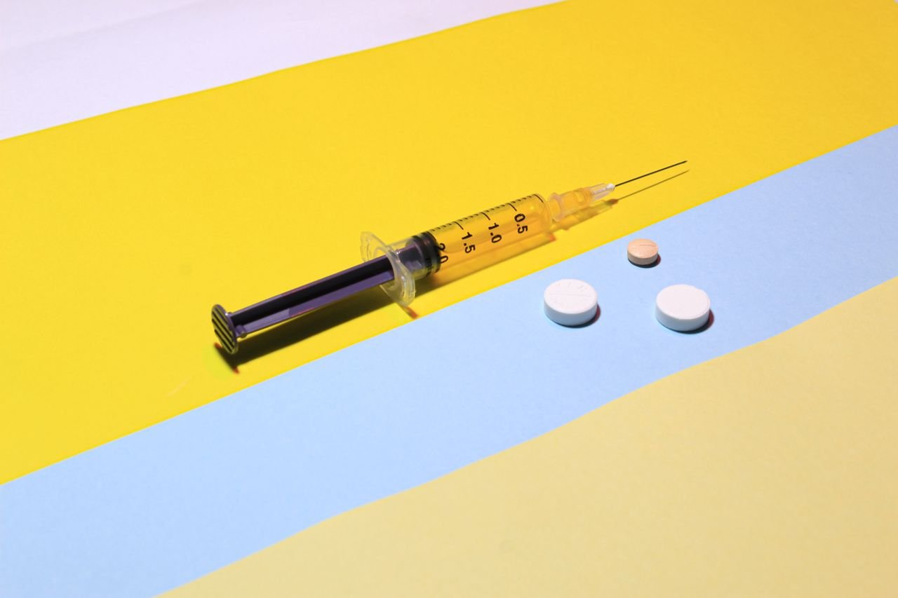 A syringe and pills on a vibrant yellow and blue background, depicting healthcare theme.